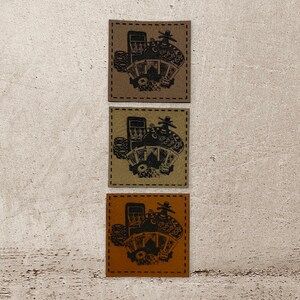 Könnte beinhalten: Drei braune Lederpatches mit einer Schwarzweißillustration einer Casinoszene. Die Szene zeigt einen Spielautomaten, Spielkarten, Würfel und Pokerchips.