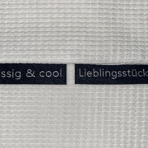 Könnte beinhalten: Zwei schwarze Stoff-Etiketten mit weißem Text. Das Etikett links lautet "lässig & cool" und das Etikett rechts lautet "Lieblingsstück".