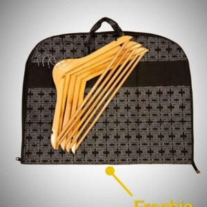 Op de afbeelding: Zwarte kledingtas met een wit geometrisch patroon en een ritssluiting. De tas is gevuld met houten hangers.