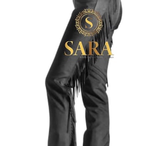 May include: Black leather chaps with fringe detailing. The chaps feature a belt and buckle closure at the waist and are designed to be worn over pants. The image includes the text "SARA" in a gold emblem.