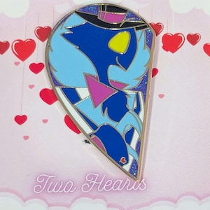 Puede incluir: Un pin de esmalte en forma de corazón con un personaje de dibujos animados azul con sombrero de copa y pajarita. El pin tiene un borde dorado y está colocado sobre un fondo rosa con corazones rojos y el texto "Two Hearts".