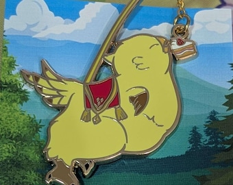 May include: A gold-colored enamel pin of a yellow bird with a red saddle, holding a pink and white cake with a strawberry on top. The bird is flying on a gold chain.