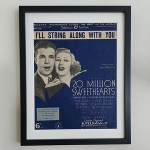 May include: A framed sheet music cover for the song "I'll String Along With You" from the 1934 film "20 Million Sweethearts". The cover features a black and white photo of a man and woman, and the title of the song is printed in large, bold letters.