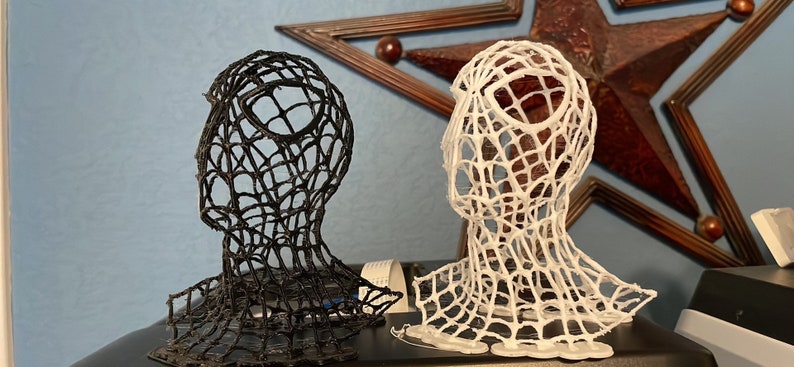 K&ouml;nnte beinhalten: Zwei 3D-gedruckte B&uuml;sten eines Kopfes mit einem Spinnennetz-Design. Eine B&uuml;ste ist schwarz und die andere ist wei&szlig;.