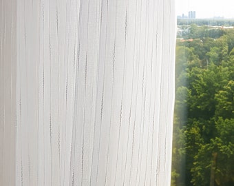 May include: Sheer white curtain with vertical, textured stripes. The curtain is partially covering a window with a view of green trees and a distant cityscape. The curtain's fabric appears lightweight and airy.