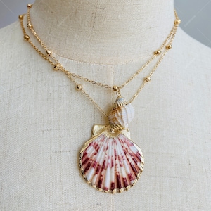 May include: A gold chain necklace with a large seashell pendant. The seashell is a scallop with a pink and white pattern. The chain is made of small gold beads.