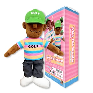 May include: A plush doll of Tyler, The Creator wearing a green cap with white GOLF text, a multi-colored striped shirt with black GOLF text, dark gray pants, and white shoes. The doll is displayed next to its packaging box labeled 25 cm.
