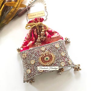 May include: A red and gold drawstring pouch bag featuring a silver-toned filigree metal overlay with embedded mirrors. The bag includes a central circular red and gold medallion, gold cord tassels, and a pearl-beaded handle. Text reads Handmade Himalaya.