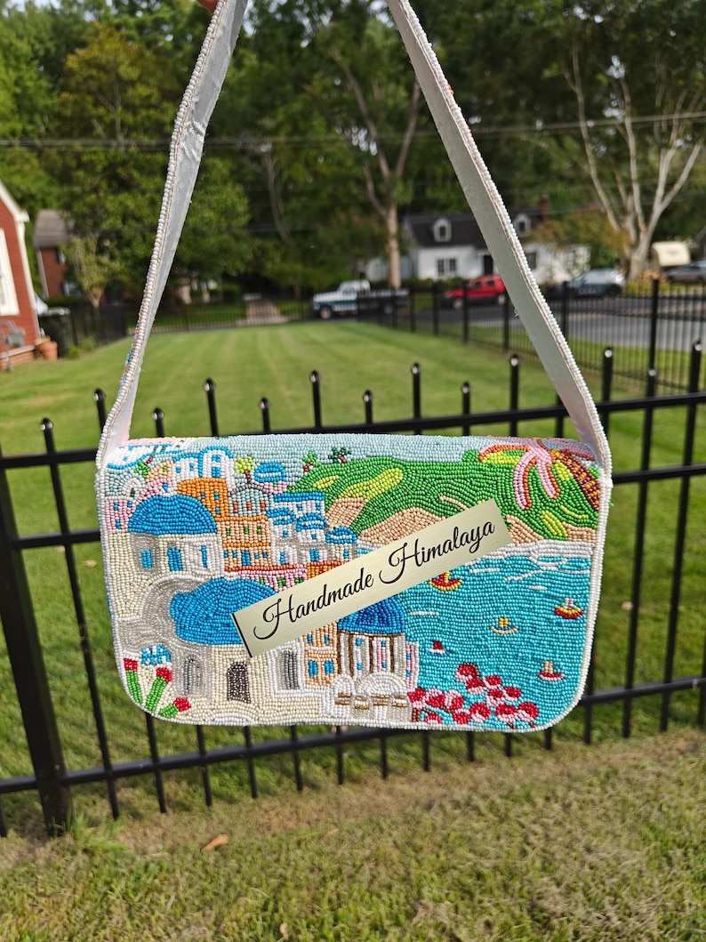 This back view of the handcrafted Santorini beaded bag displays a colorful continuation of the coastal landscape with white and blue Grecian buildings nestled into a green hillside overlooking the bright blue Mediterranean sea. This unique beaded purse captures the spirit of a summer vacation with its artistic beach-inspired beadwork. A stylish accessory for resort fashion and travel, this blue and white handbag makes a special Christmas gift.