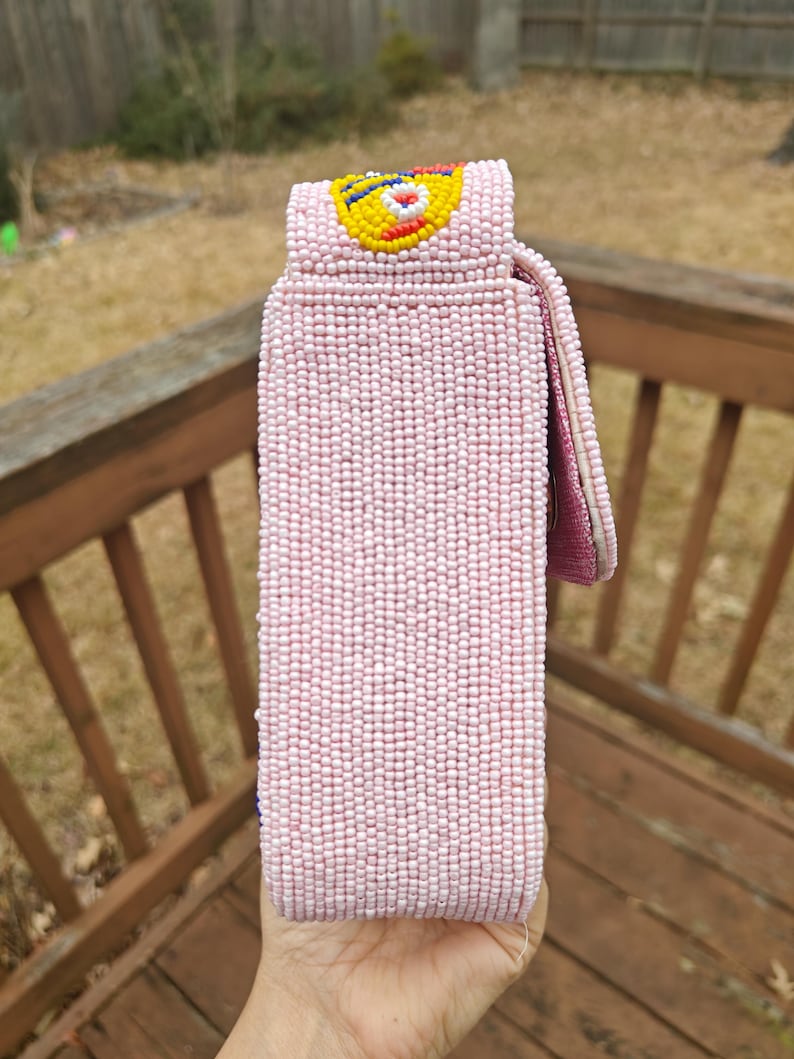 Full side view showing the depth of the sardines beaded bag and the attachment point of the beaded strap. This pink seed bead bag is built with a blend of canvas and suede for durability. The image displays the uniform bead patterns that cover every inch of the novelty beaded purse. As a handmade Indian beaded bag, it offers a sophisticated yet playful silhouette, making it an excellent choice for a summer beach outing or a unique gift for her.