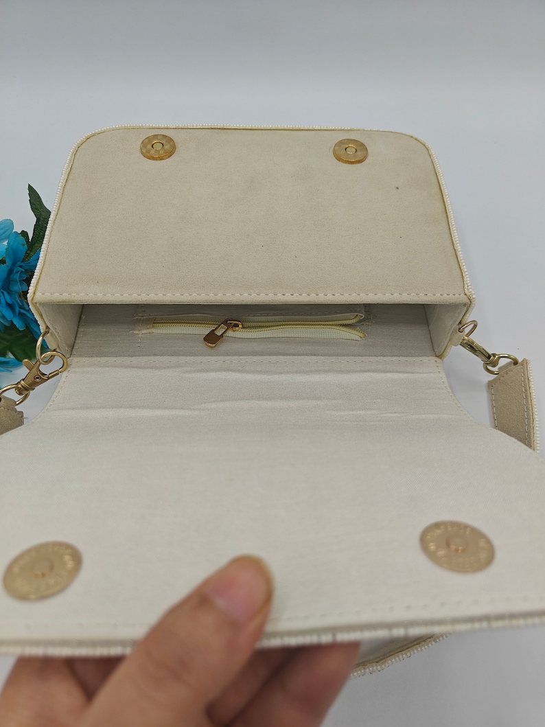 Handmade beaded handbag interior with ivory fabric lining and zip pocket compartment, artisan evening purse inside view showing magnetic snap closure and structured storage space, elegant beaded shoulder bag interior with secure zipper pocket for cards, cash or small essentials, luxury handcrafted evening handbag inside detail, bridal or wedding guest purse storage compartment, designer handmade beaded bag interior construction.