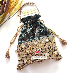 May include: A drawstring pouch bag featuring a dark green fabric top with a silver floral pattern and a gold-toned metal base with intricate filigree, embedded mirrors, and colorful accents. The bag includes a gold chain handle and tassel ties.
