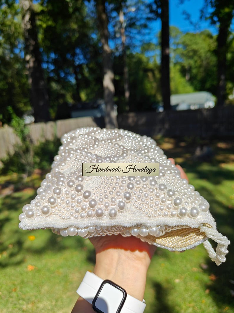 A side-angle view of the open handbag reveals the generous depth of the interior gusset and the sturdy construction of the pearl-encrusted flap. The image shows the internal lining expanded, proving it can comfortably hold a smartphone and beauty essentials. The transition from the heavy exterior beadwork to the smooth, protective fabric lining is seamless and high-quality.