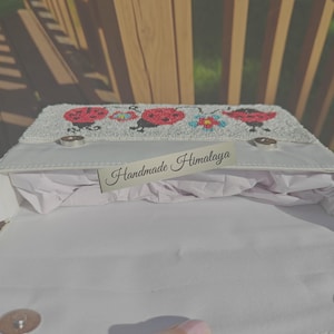 Open top-down view of a ladybug beaded bag displaying interior lining and silver magnetic clasp closure. White cotton fabric lining inside main compartment stuffed with protective paper. Beadwork fold-over flap shows red ladybug designs along edge. Rectangular structure designed as a compact ladybug shoulder bag for essential phone, cards, and small items.