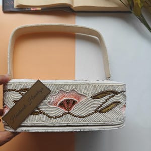 Handmade floral beaded handbag side view with ivory seed bead embroidery and peach flower design, artisan shoulder bag featuring gold leaf beadwork pattern and structured top handle, elegant handcrafted beaded purse with intricate botanical embroidery, luxury evening handbag for wedding guest, bridal shower, spring party or formal event, unique cottagecore floral purse gift for her, designer artisan beaded fashion accessory.