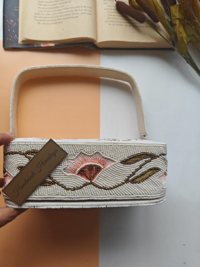 Handmade floral beaded handbag side view with ivory seed bead embroidery and peach flower design, artisan shoulder bag featuring gold leaf beadwork pattern and structured top handle, elegant handcrafted beaded purse with intricate botanical embroidery, luxury evening handbag for wedding guest, bridal shower, spring party or formal event, unique cottagecore floral purse gift for her, designer artisan beaded fashion accessory.