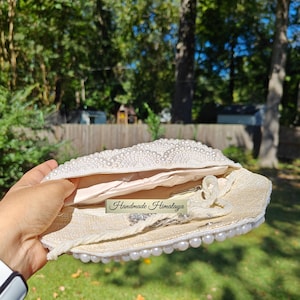 A detailed interior view shows the silver-tone chain strap and beaded strap tucked inside the linen-lined compartment to illustrate scale and versatility. The image captures the fine weave of the inner fabric and the durable metal hardware. The contrast between the organic linen and the opulent, polished pearls highlights the bag's dual nature as a practical tool and a fashion statement.
