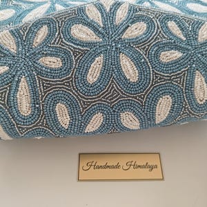 An extreme close-up of the Blue Flower Bag focuses on the individual ivory and cornflower blue beads, illustrating the collectible beadwork quality. The shimmering silver thread work between the petals mirrors the look of porcelain print or fine china. Regarding scale, the beads are tiny seed-sized elements, proving the hundreds of hours of labor required to create this something blue gift for a bride, bridesmaid, or mother of the bride.