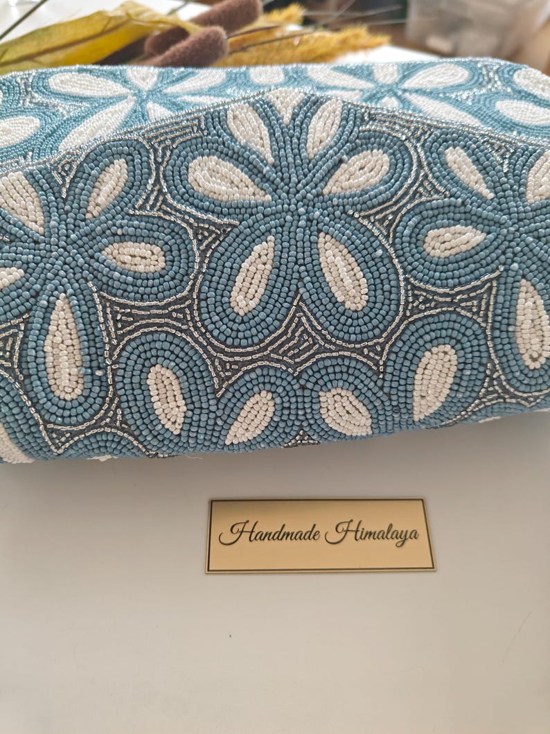An extreme close-up of the Blue Flower Bag focuses on the individual ivory and cornflower blue beads, illustrating the collectible beadwork quality. The shimmering silver thread work between the petals mirrors the look of porcelain print or fine china. Regarding scale, the beads are tiny seed-sized elements, proving the hundreds of hours of labor required to create this something blue gift for a bride, bridesmaid, or mother of the bride.