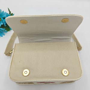 Beaded handbag interior view with ivory fabric lining and magnetic snap closure, handmade artisan purse inside compartment showing clean spacious design, structured evening bag interior with soft textile lining and secure flap closure, elegant handcrafted beaded shoulder bag inside detail, bridal or wedding guest handbag storage space for phone, makeup and essentials, luxury handmade purse interior construction.