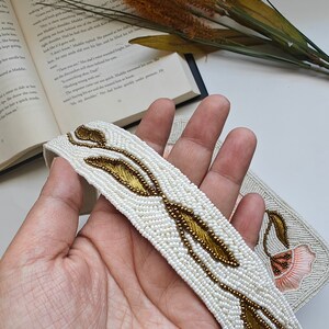 Beaded handbag strap detail handmade with white seed bead embroidery and gold leaf pattern, artisan shoulder bag handle featuring intricate beadwork design on ivory fabric, elegant handmade beaded purse strap for floral evening handbag, luxury handcrafted beaded shoulder strap with botanical embroidery, unique artisan bag handle for bridal purse, wedding guest handbag or formal evening bag, designer beaded fashion accessory detail.