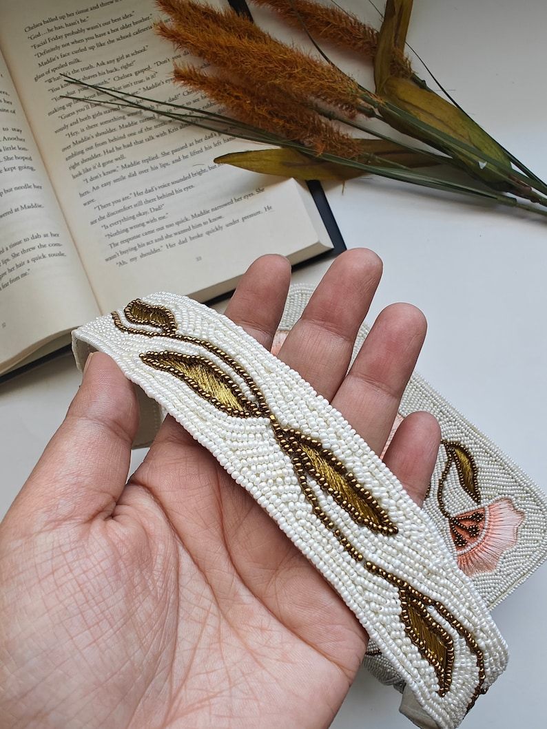 Beaded handbag strap detail handmade with white seed bead embroidery and gold leaf pattern, artisan shoulder bag handle featuring intricate beadwork design on ivory fabric, elegant handmade beaded purse strap for floral evening handbag, luxury handcrafted beaded shoulder strap with botanical embroidery, unique artisan bag handle for bridal purse, wedding guest handbag or formal evening bag, designer beaded fashion accessory detail.