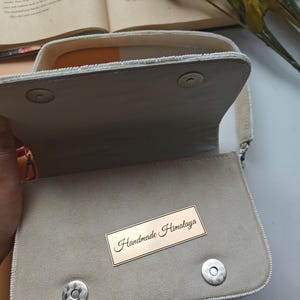 Handmade beaded handbag interior view with soft ivory fabric lining and magnetic snap closure, artisan evening purse inside compartment showing spacious storage for phone, wallet and makeup essentials, elegant handcrafted beaded shoulder bag interior with structured design and secure flap closure, luxury bridal or wedding guest handbag inside detail, designer handmade purse construction, artisan evening clutch interior.