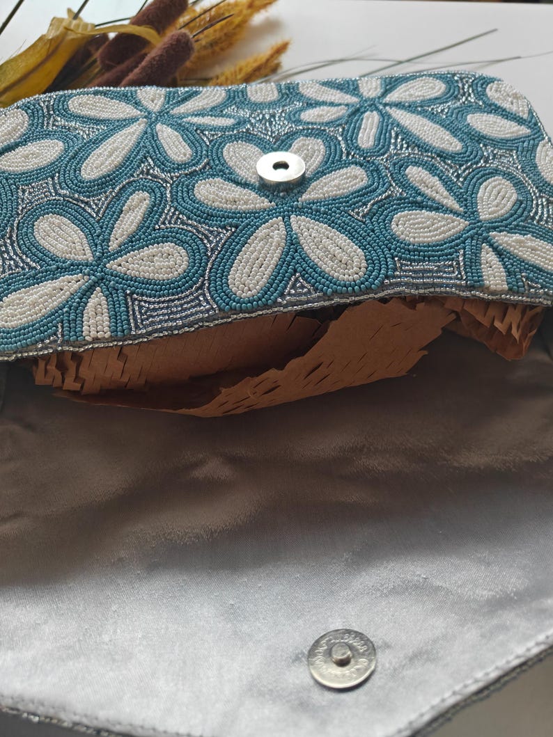 This interior view reveals the magnetic snap closure and the smooth satin lining of the Dusty Blue Wedding accessory, showcasing the high-quality finish. The underside of the flap continues the embroidered flower bag motif, ensuring beauty from every angle. For scale, the open compartment is shown to be deep enough to securely fit a smartphone (Iphone Pro max models), a slim wallet, and daily essentials, proving its utility as a functional Spring Formal Bag.