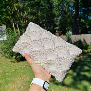 The back view of the beaded purse is held horizontally, revealing a flawless and continuous field of concentric pearl circles. There are no interruptions in the intricate beadwork, demonstrating a commitment to 360-degree luxury. The texture appears incredibly tactile and rich, with the natural light defining each individual pearl to showcase the scale and depth of the artisan construction.