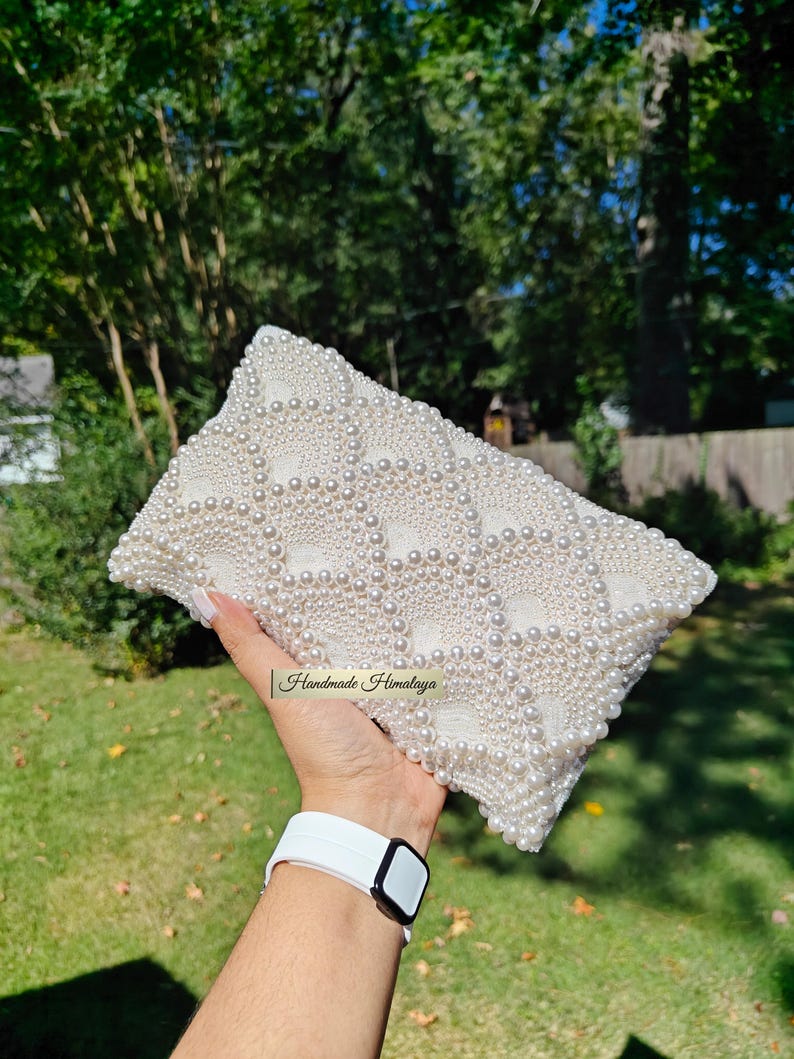 The back view of the beaded purse is held horizontally, revealing a flawless and continuous field of concentric pearl circles. There are no interruptions in the intricate beadwork, demonstrating a commitment to 360-degree luxury. The texture appears incredibly tactile and rich, with the natural light defining each individual pearl to showcase the scale and depth of the artisan construction.