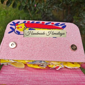 Interior view of the open pink quirky handbag revealing the magnetic closure and pink fabric lining. This handmade Indian beaded bag shows the single compartment currently filled with packing material to maintain its shape. The artisan beaded bag construction combines canvas and jute with high-quality hardware. This view emphasizes the functionality of the small clutch bag, designed to keep essentials safe while maintaining its coastal aesthetic.