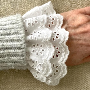 May include: White cotton lace cuff with a scalloped edge and eyelet detailing. The cuff is layered and has a delicate, feminine look.