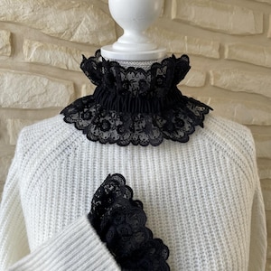 May include: A white sweater with a black lace collar and matching lace cuffs.