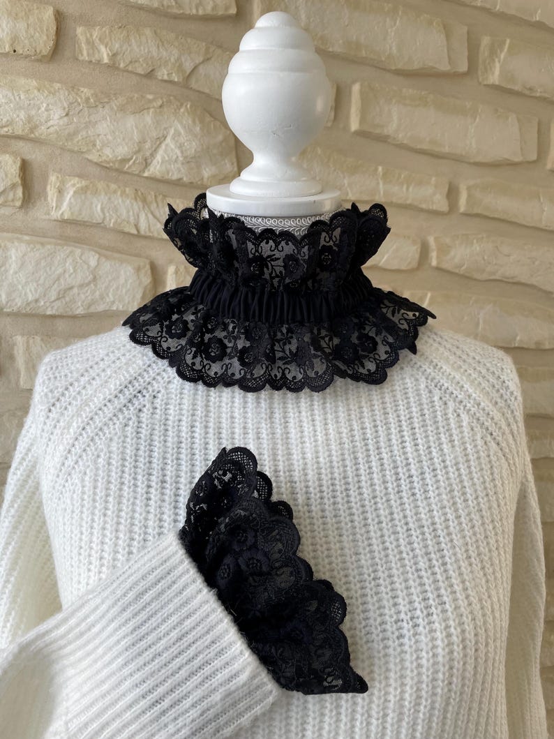 May include: A white sweater with a black lace collar and matching lace cuffs.
