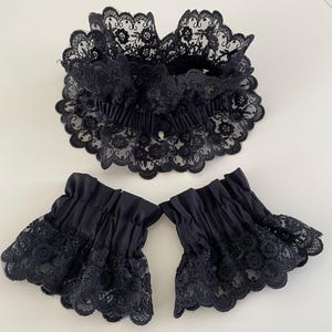 May include: A set of black lace cuffs and a matching collar. The cuffs are made of a black fabric with a lace trim. The collar is made of a black lace fabric.