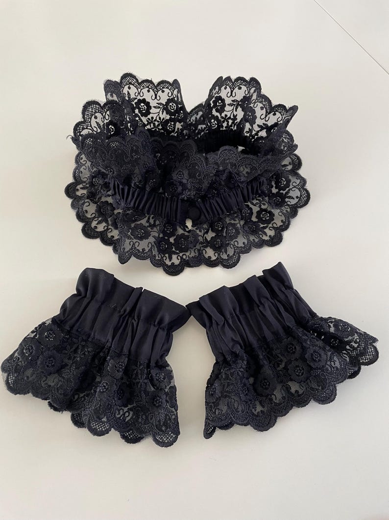 May include: A set of black lace cuffs and a matching collar. The cuffs are made of a black fabric with a lace trim. The collar is made of a black lace fabric.