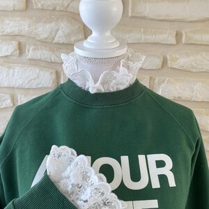 May include: A green sweatshirt with the text "Amour Cafe" printed on the front. The sweatshirt has white lace trim around the neck and on the sleeves.