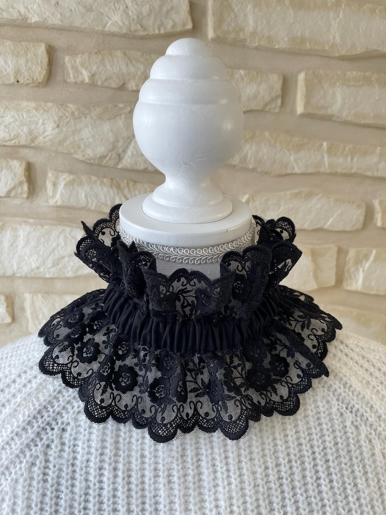 May include: Black lace collar with a scalloped edge and floral pattern. The collar is displayed on a white mannequin head.
