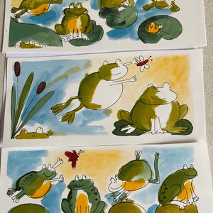 Peut inclure: Trois aquarelles de grenouilles sur des nénuphars. La première peinture montre quatre grenouilles, deux vertes et deux jaunes, avec des papillons rouges. La deuxième peinture montre deux grenouilles, une verte et une blanche, avec un papillon rouge. La troisième peinture montre quatre grenouilles, deux vertes et deux jaunes, avec un papillon rouge.