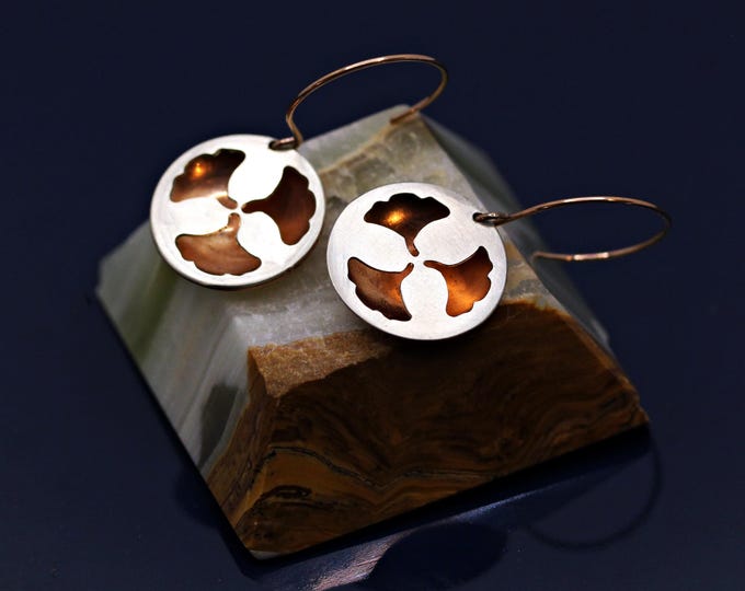 Round hoop earrings featuring a ginkgo leaf motif in vibrant orange and elegant silver.