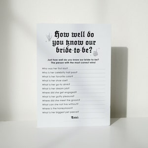 Peut inclure: Une carte de jeu imprimable avec le texte "How well do you know our bride-to-be?" et une liste de questions pour tester &agrave; quel point quelqu'un conna&icirc;t la future mari&eacute;e. La carte a un th&egrave;me d'Halloween effrayant avec une main de squelette et des &eacute;toiles.