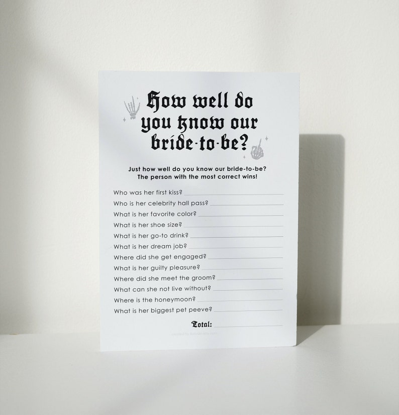 Peut inclure: Une carte de jeu imprimable avec le texte "How well do you know our bride-to-be?" et une liste de questions pour tester &agrave; quel point quelqu'un conna&icirc;t la future mari&eacute;e. La carte a un th&egrave;me d'Halloween effrayant avec une main de squelette et des &eacute;toiles.