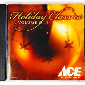 May include: A compact disc in a clear plastic jewel case titled Holiday Classics Volume One. The cover art features a warm, glowing orange and yellow background with dark star-shaped accents and the Ace The helpful place logo in the corner.