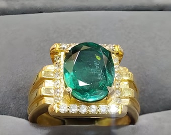 May include: A gold ring featuring a large, oval-cut emerald gemstone. The emerald is surrounded by a halo of small diamonds, and the ring has a textured, ribbed band. The ring is set against a gray background.