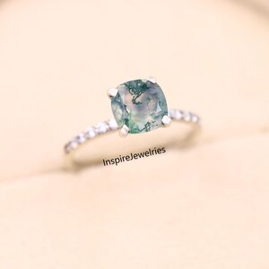 May include: A silver ring with a square-cut, moss agate gemstone. The ring band is adorned with small, clear stones. The text "InspireJewelries" is visible at the bottom of the image. The gemstone has green and white inclusions.