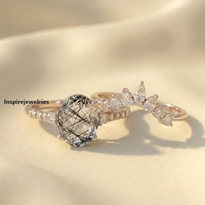 May include: Three rose gold rings. The primary ring features an oval-cut, clear gemstone with black inclusions. A second ring has small, clear stones. The third ring is a curved band with marquise-cut stones. The text "Inspirejewelries" is visible.