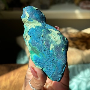 May include: A blue and green malachite crystal with a rough, textured surface. The crystal is irregularly shaped and has a natural, organic look.