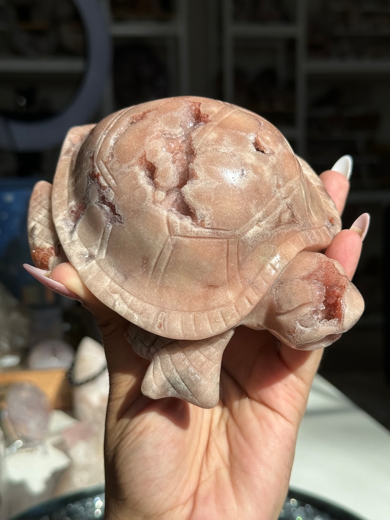 May include: A pink and white carved turtle figurine made of rose quartz. The turtle has a detailed shell and a smooth, polished finish.