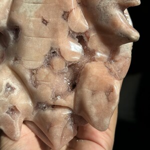 May include: A pink and white carved stone with a rough, textured surface. The stone has a natural, organic shape and is covered in small, white crystals.