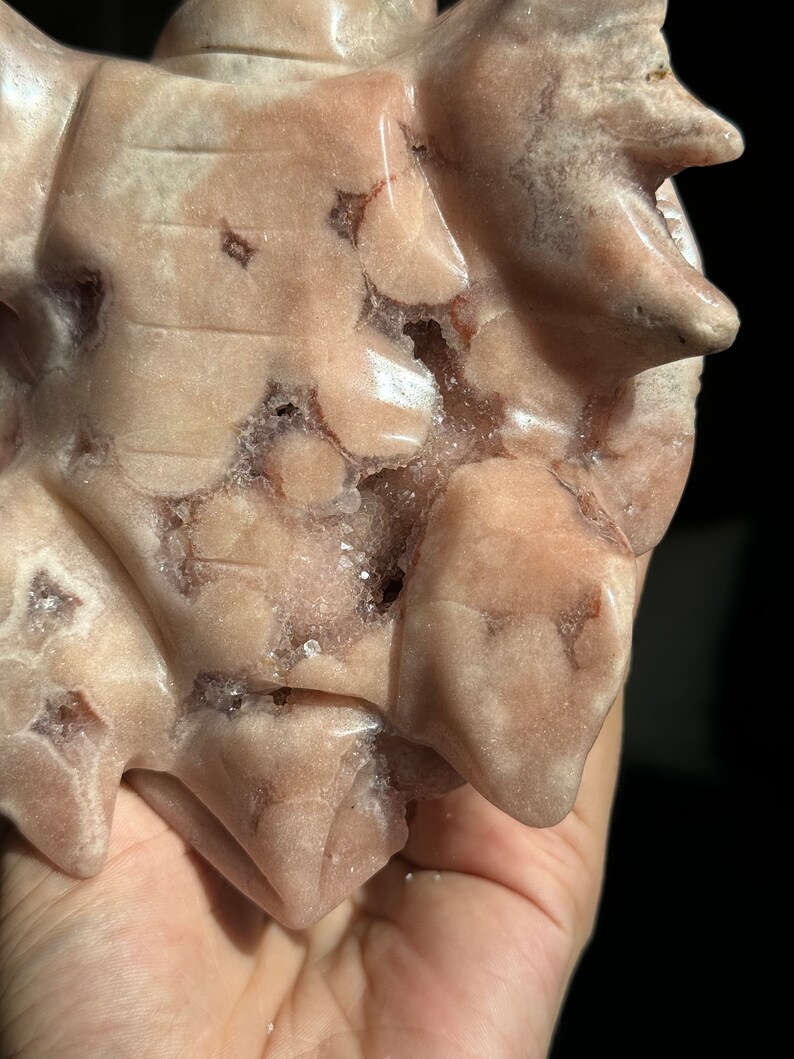 May include: A pink and white carved stone with a rough, textured surface. The stone has a natural, organic shape and is covered in small, white crystals.